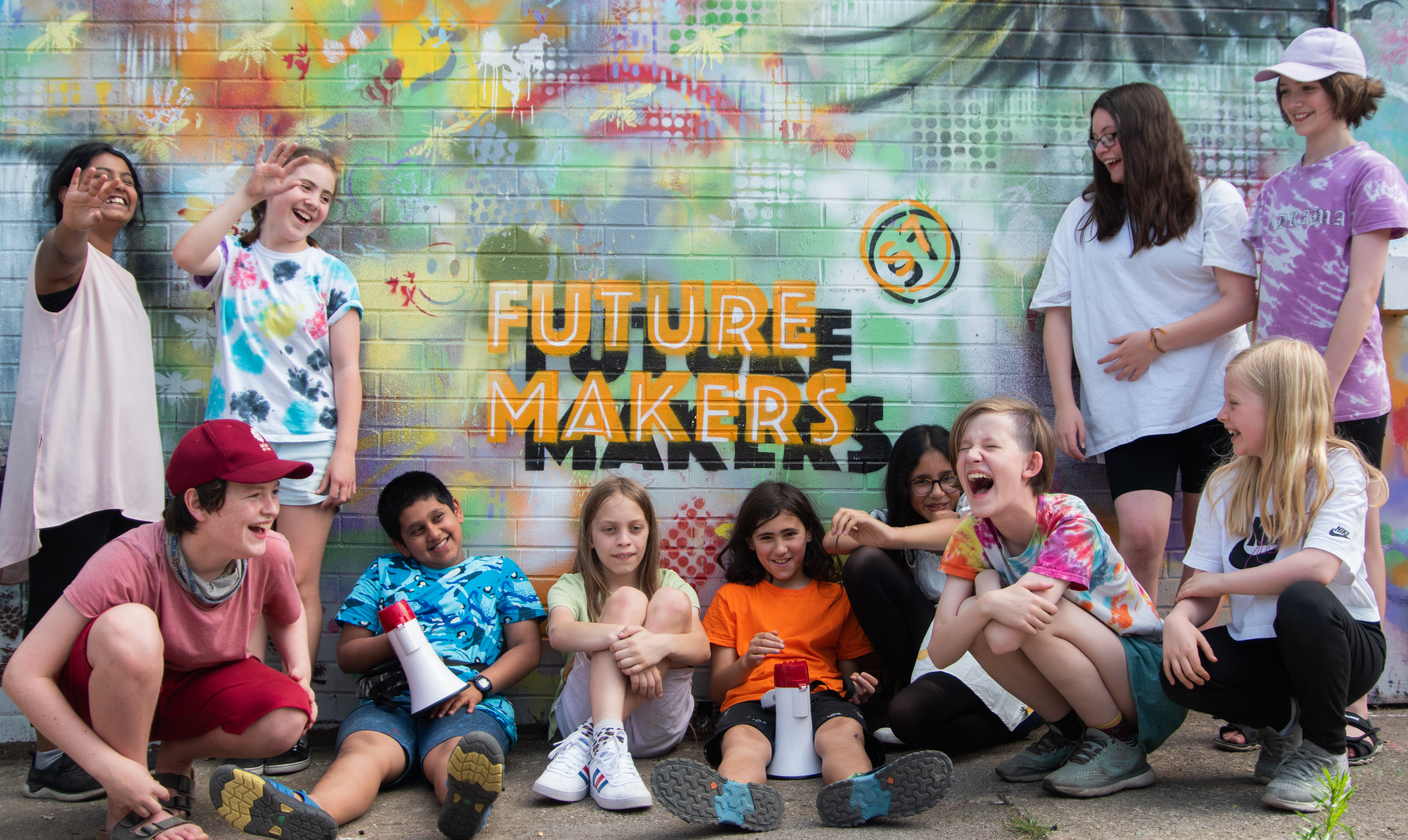 11 young people sat and stood against a wall of graffiti, the logo for "Future Makers S7" at the centre